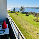 Balkon mit Tisch und Stühlen bietet Blick auf Grünfläche und Wasser.
