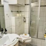 Badezimmer mit Dusche, Waschbecken und Toilette. Weiße Fliesen und Handtücher.