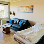 Wohnraum mit Sofa, Bett und Balkonblick. Wandbilder und Holztisch.