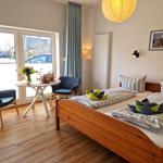 Ein Schlafzimmer mit Doppelbett, zwei Stühlen und Tisch. Durchgangstür mit Blick nach draußen.