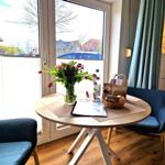 Rundtisch mit Blumen, Brot und Getränk vor großem Fenster.