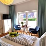 Ein Schlafzimmer mit Bett, TV, Tisch und Stühlen. Durchgang zum Balkon mit Blick auf die Straße.