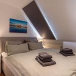 Schlafzimmer mit Dachschrägen, Bett mit Kissen und Handtüchern, Nachttisch mit Lampe und Wandbild.