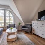 Wohnzimmer mit Schlafsofa, zwei Sesseln, Couchtisch und Fernseher auf Schrank
