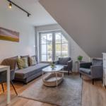 Wohnbereich mit Sofa, Sesseln, Esstisch und TV-Schrank unter Dachschräge.