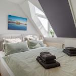 Schlafzimmer mit Dachschrägen, Bett mit Kissen und Handtüchern, Fenster und Wandbild.