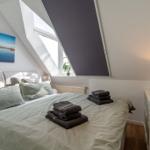 Schlafzimmer mit Dachschrägen, Bett mit Handtüchern, Fenster und Wandbild.