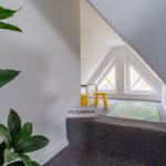 Kinderzimmer mit Spielteppich, gelben Hockern und Dreiecksfenstern unter Dachschrägen.