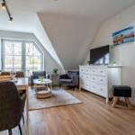 Wohn- und Essbereich mit Holzboden, TV-Schrank und Fenster zur Terrasse.