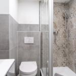 Badezimmer mit Dusche, Toilette und Waschbecken. Wandfliesen in Grau und Muster.