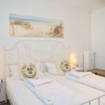 Schlafzimmer mit Doppelbett, Wandbild und Nachttischen mit Lampen.