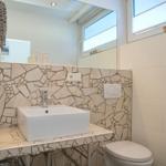 Badezimmer mit Waschbecken, Spiegel und Toilette. Wandverkleidung aus Mosaikfliesen.