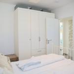 Schlafzimmer mit weißem Bett, Kleiderschrank und Lampe.