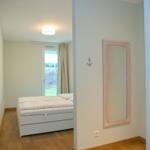 Schlafzimmer mit weißem Bett, Spiegel und Fenster zum Garten.