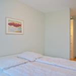Schlafzimmer mit Bett, Wandbild und Blick in einen Flur.