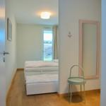 Schlafzimmer mit Bett, Spiegel und Stuhl. Tür führt ins Zimmer.