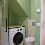 Badezimmer mit Waschmaschine, Toilette und Dusche mit Glaswand.