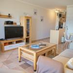 Wohnzimmer mit Sofa, Couchtisch und Fernseher. Essbereich mit Tisch und Stühlen im Hintergrund.