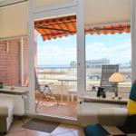 Wohnraum mit Blick auf Balkon und Meeresblick. Balkon mit Tisch, Stühlen und Markise.