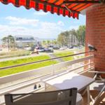 Terrasse mit Tisch, Stühlen und rotem Markisen, Blick auf Grünfläche und Strand.