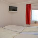 Zimmer mit Doppelbett, Fernseher und Fenster mit roten Vorhängen.