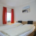 Schlafzimmer mit Doppelbett, roten Vorhängen und Wandbild.