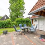 Terrace with table and chairs, garden, house with door and window.