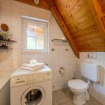 Bathroom with washing machine, toilet, and skylight under wooden ceiling.