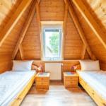 Two single beds with nightstands and lamps under wooden ceiling with window.