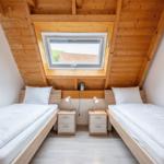 Two single beds under wooden roof with skylight and nightstands.