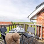 Terrasse mit Tisch, Stühlen und Teeservice. Blick auf grüne Wiesen und rote Dächer.