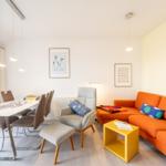 Wohn- und Essbereich mit orangefarbenem Sofa, Esstisch und Stühlen sowie Wandbildern.
