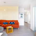 Wohnbereich mit orangefarbenem Sofa, gelbem Beistelltisch und Fernseher.