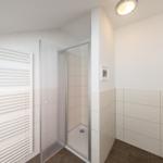 Badezimmer mit Dusche und Heizkörper an der Wand.