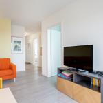 Wohnzimmer mit orangefarbenem Sofa, Fernseher und Holzmöbeln. Blick in den Flur.