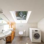 Badezimmer mit Waschmaschine, Toilette und Dachfenster. Holzregal und Spiegel.