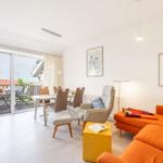 Wohn- und Essbereich mit Balkon, orange Sofa und Esstisch mit Stühlen.