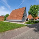 Moderne Ferienhaus mit rotem Dach und grünem Garten. Nebenhaus und Parkplatz sind sichtbar.
