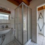 Badezimmer mit Dusche, Waschbecken und Spiegel. Holzdecken und Fliesen.
