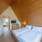 Schlafzimmer mit Holzwand und Doppelbett. TV und Nachttisch sind vorhanden.