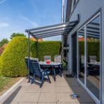 Terrasse mit Sitzgruppe unter Markise. Hinterhof mit Hecke und Rasen.