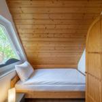 Schlafzimmer mit Dachschrägen, Holzwand, Fenster und Bett.