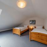 Zwei Einzelbetten, Fenster und Nachttisch in einem Dachzimmer.