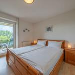 Doppelbett mit Holzrahmen, zwei Nachttische mit Lampe, Balkon mit Gartenblick.