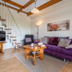 Wohnzimmer mit Sofa, Couchtisch und TV. Treppenhaus führt zur oberen Etage.