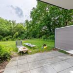 Terrace with table, chair, and garden. Background: green area and trees.