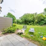 Backyard with lounge chairs and childrens toys on grass area beside house wall.