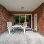 Terrace with table and two chairs, red brick wall, glass door and door.