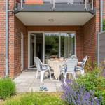 Terrasse mit Tisch und Stühlen, umgeben von Pflanzen und einem Balkon.