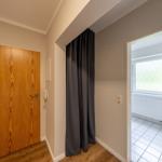 Flur mit Holztür und Vorhang, Blick in Bad mit Toilette und Fenster.